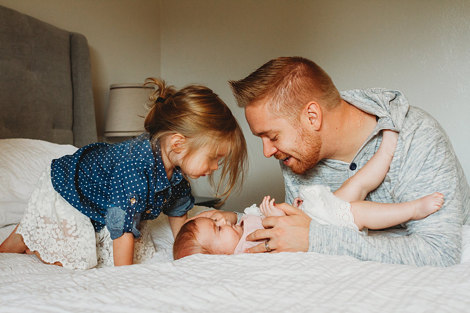 Candid photo of dad with baby and toddler on bed