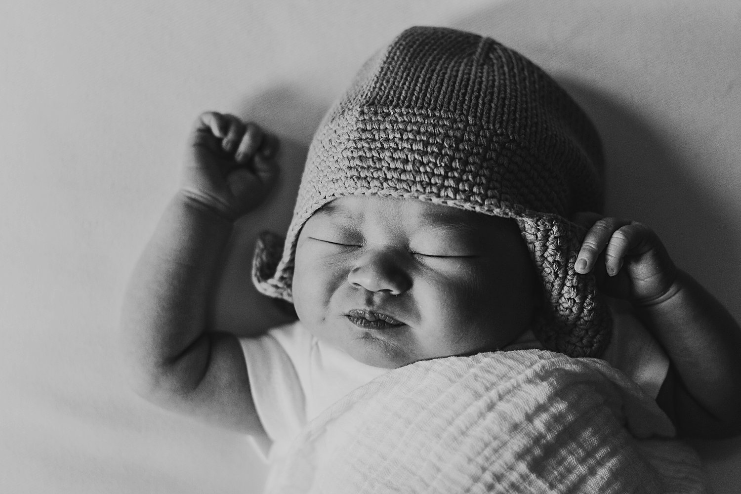 Newborn baby swaddled wearing hat and stretching