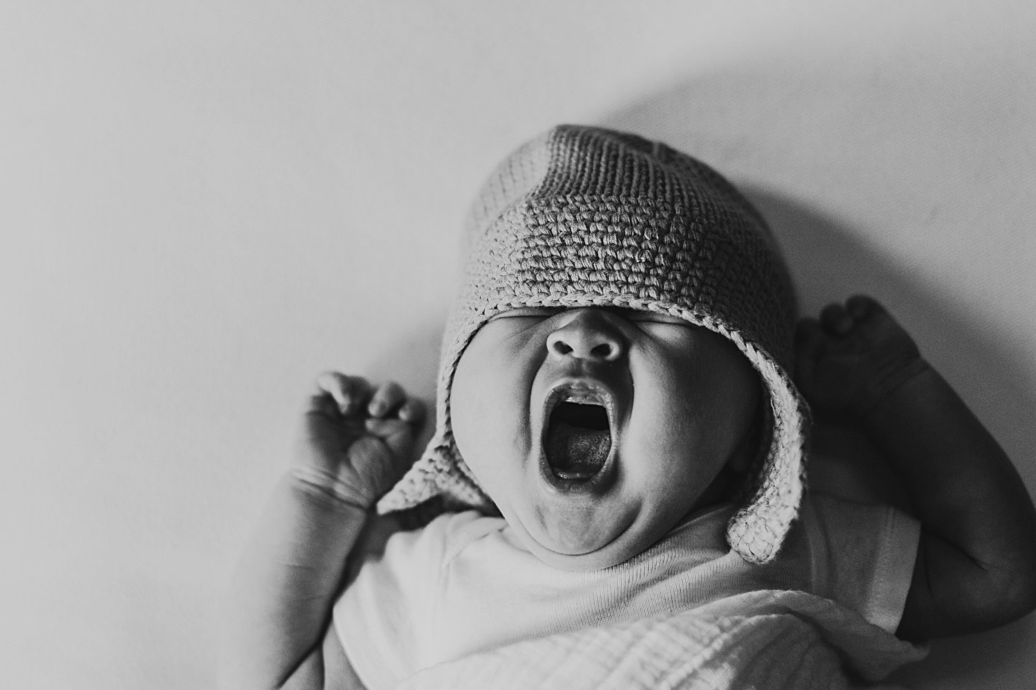 Newborn baby yawning very wide in swaddle and hat