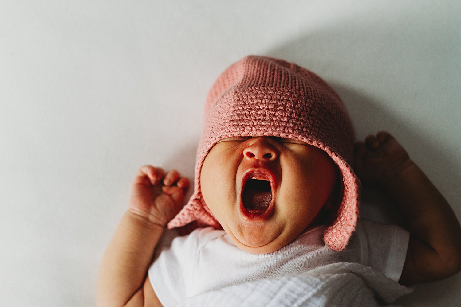 Newborn baby yawning very wide in swaddle and hat