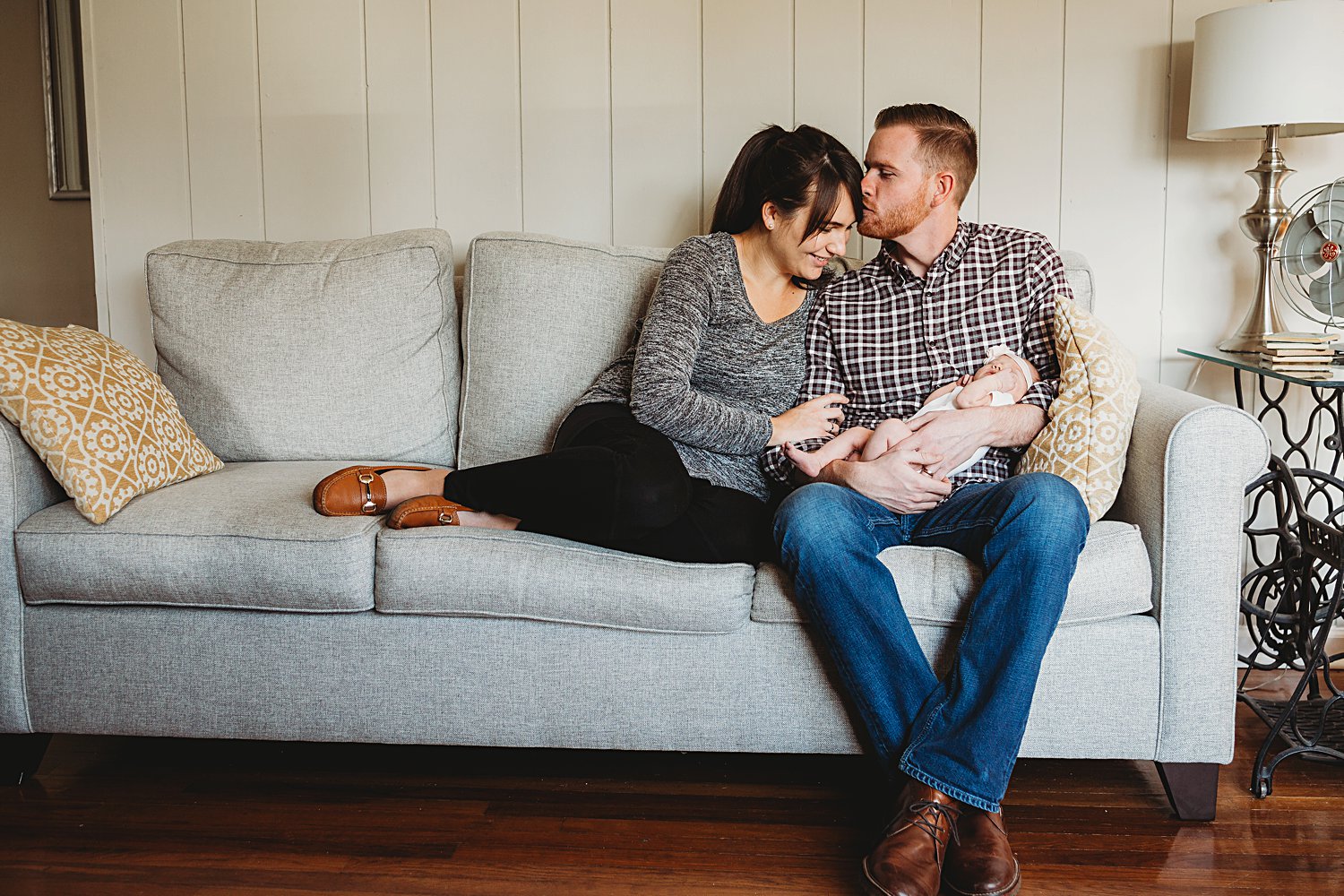Lifestyle photo of couple sitting on couch in their home with newborn baby girl