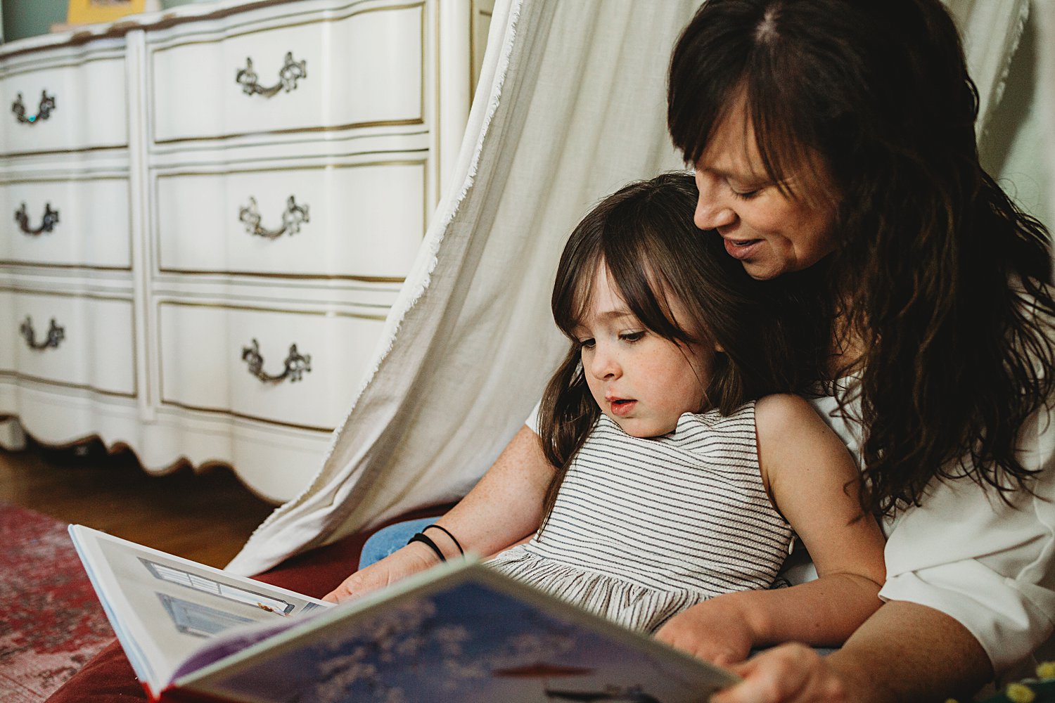 Mom and young daughter reading book together