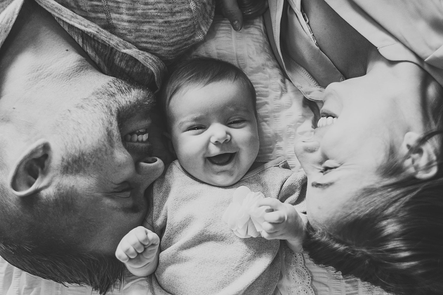 Laughing baby between mom and dad laying on bed